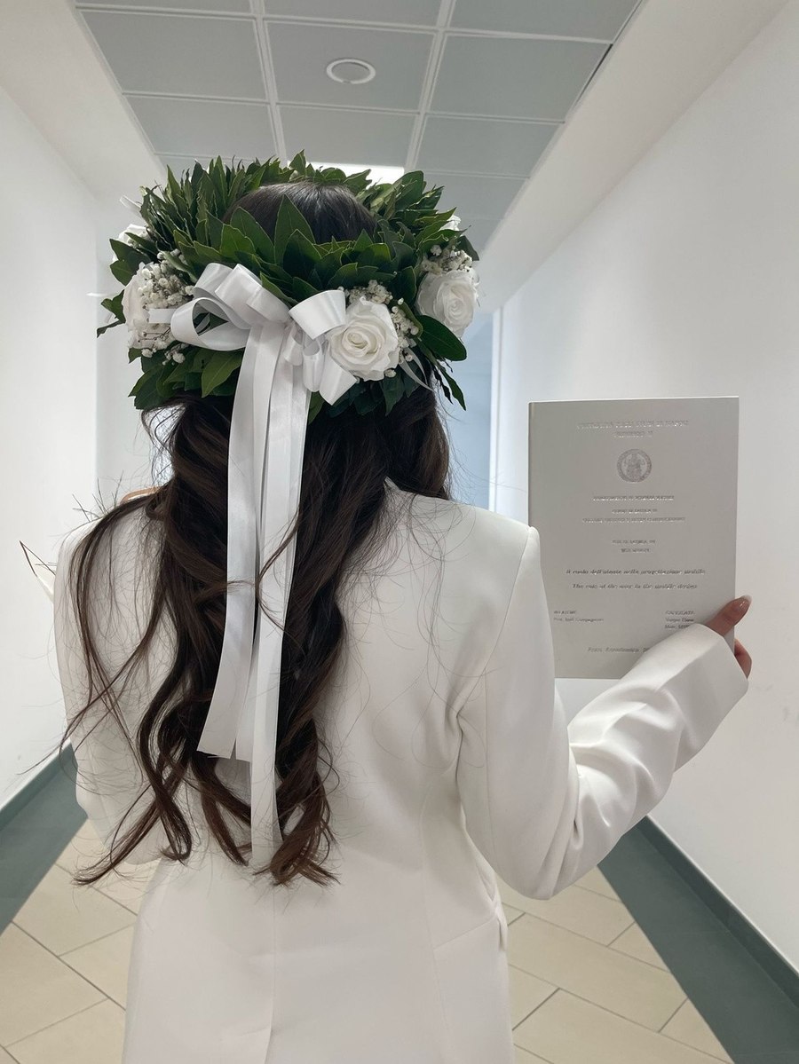 Elena Vargas from behind wearing a graduation flower crown, holding her diploma
